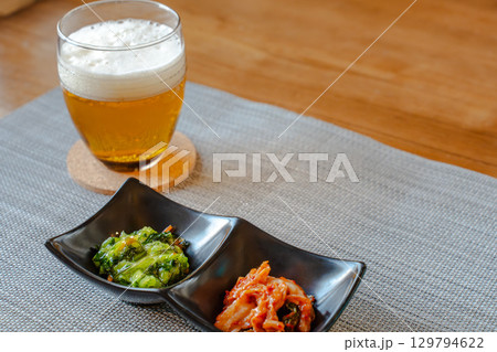 ビールとキムチや青菜のおつまみを並べた家庭的な晩酌の食卓 129794622