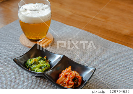 ビールとキムチや青菜のおつまみを並べた家庭的な晩酌の食卓 129794623