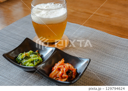 ビールとキムチや青菜のおつまみを並べた家庭的な晩酌の食卓 129794624