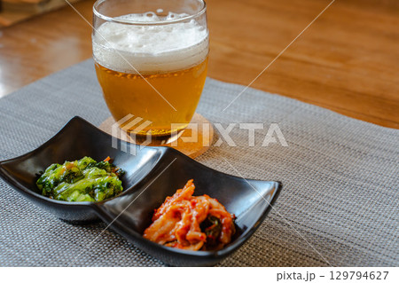 ビールとキムチや青菜のおつまみを並べた家庭的な晩酌の食卓 129794627