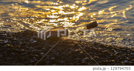 Message in a bottle washing ashore at sunset on a pebble beach 129794703