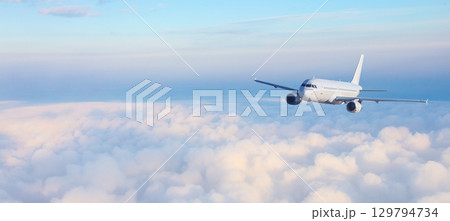 White passenger airplane flying above clouds at sunrise White passenger airplane flying above clouds at sunrise 129794734