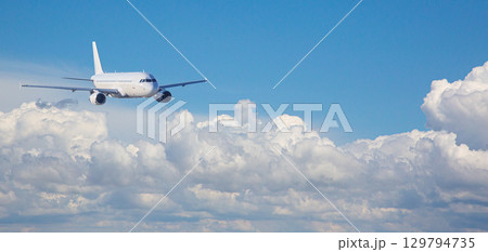 White passenger airplane flying above beautiful cloudscape on sunny day White passenger airplane flying above beautiful cloudscape on sunny day 129794735