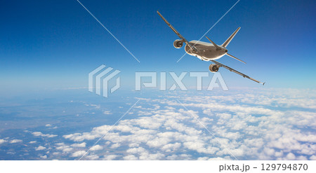 White passenger airplane flying in cloudy blue sky 129794870