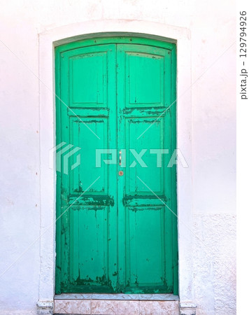 Old green wooden door on white wall with peeling paint Old green wooden door on white wall with peeling paint 129794926