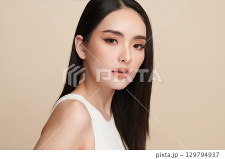 A beautiful young Asian woman with clean, fresh skin against a beige background. Skincare, facial treatment, cosmetology, beauty, and spa. An elegant portrait of an Asian woman. A beautiful young Asian woman with clean, fresh skin against a beige background. Skincare, facial treatment, cosmetology, beauty, and spa. An elegant portrait of an Asian woman. 129794937