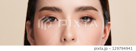 Close-up shot of beautiful Asian woman eyes on beige background. Close-up shot of beautiful Asian woman eyes on beige background. 129794941