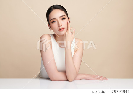 A beautiful young Asian woman with clean, fresh skin against a beige background. Skincare, facial treatment, cosmetology, beauty, and spa. An elegant portrait of an Asian woman. 129794946