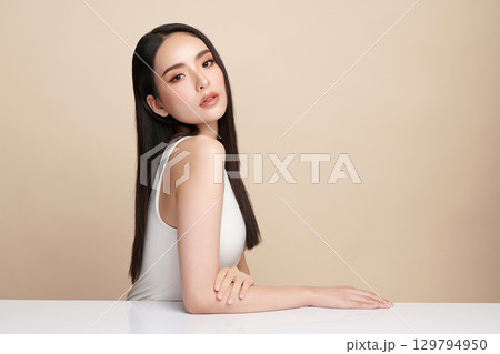 A beautiful young Asian woman with clean, fresh skin against a beige background. Skincare, facial treatment, cosmetology, beauty, and spa. An elegant portrait of an Asian woman. A beautiful young Asian woman with clean, fresh skin against a beige background. Skincare, facial treatment, cosmetology, beauty, and spa. An elegant portrait of an Asian woman. 129794950