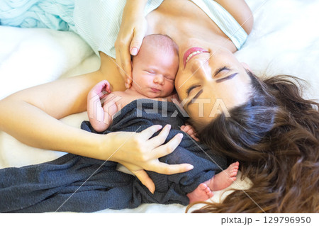 Mother cradles newborn baby with joy in a cozy setting during daytime 129796950