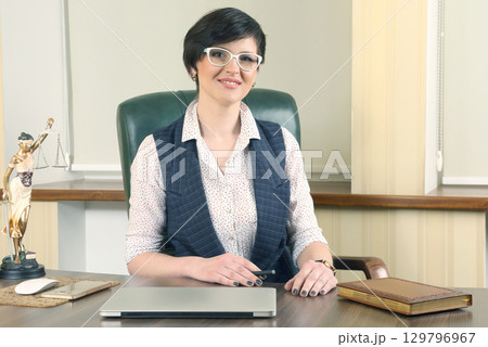 Professional woman at an office desk with laptop and law-themed decor Professional woman at an office desk with laptop and law-themed decor 129796967
