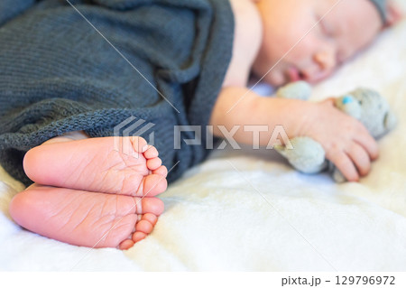 Baby peacefully sleeping while clutching a small toy in cozy surroundings 129796972
