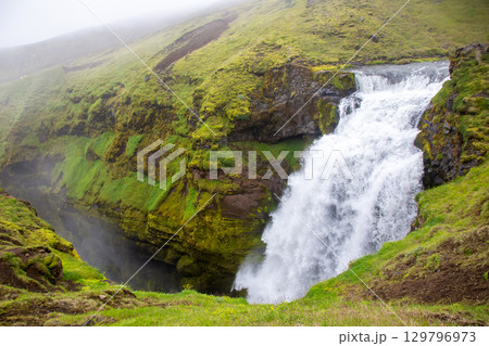Majestic waterfall cascades through lush green landscape in Iceland's natural beauty 129796973