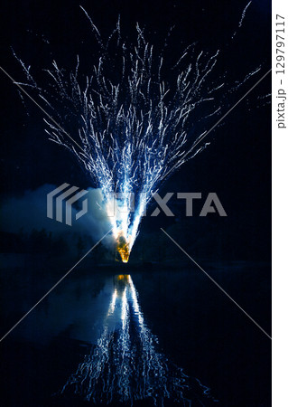 Bright fireworks illuminate the night sky over a calm lake during a festive celebration Bright fireworks illuminate the night sky over a calm lake during a festive celebration 129797117