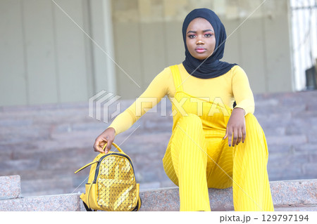 Elegant African woman in bright yellow outfit poses stylishly outdoors 129797194