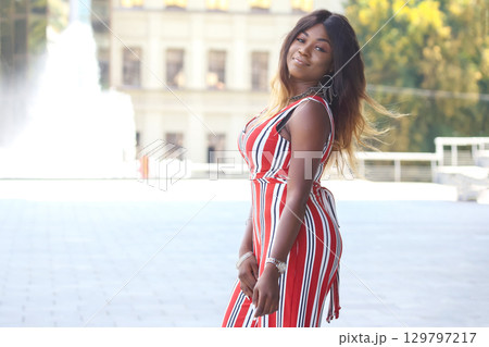 Beautiful African woman in stylish striped outfit poses confidently outdoors in the city Beautiful African woman in stylish striped outfit poses confidently outdoors in the city 129797217