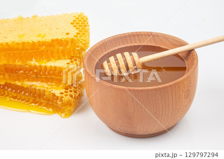 Sweet honey drizzled from a wooden dipper into a bowl beside fresh honeycomb 129797294