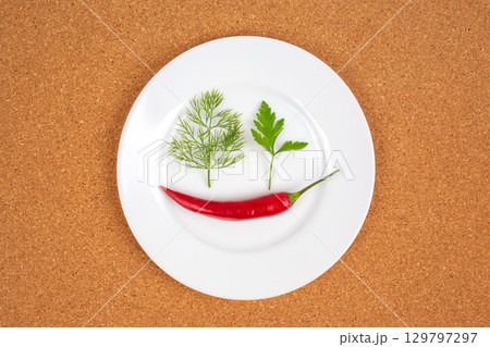 Bright red chili pepper and fresh green herbs arranged on a white plate for culinary art Bright red chili pepper and fresh green herbs arranged on a white plate for culinary art 129797297