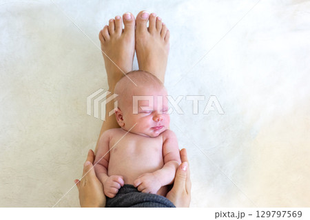 Newborn baby resting peacefully on a parent's legs in a cozy indoor setting Newborn baby resting peacefully on a parent's legs in a cozy indoor setting 129797569
