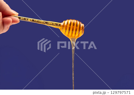Honey drips from a wooden dipper against a vibrant blue background Honey drips from a wooden dipper against a vibrant blue background 129797571