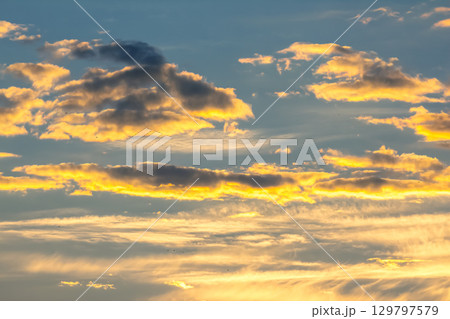 Vibrant sunset sky with clouds illuminated in golden hues over the horizon 129797579