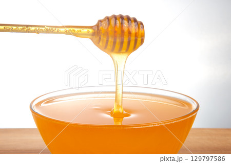 Smooth honey dripping from a wooden dipper into a clear bowl, perfect for sweetening beverages 129797586