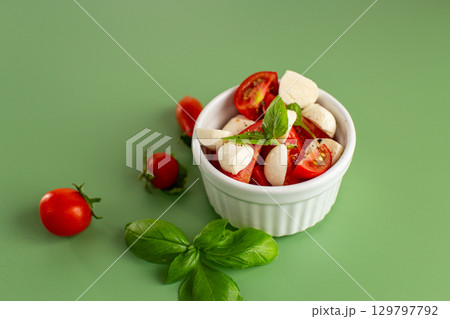 italian caprese salad in a white ceramic bowl on a green background 129797792