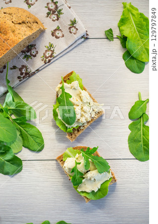 Close-up of a sandwich with herring and salad leaves on a light wooden table Close-up of a sandwich with herring and salad leaves on a light wooden table 129797849