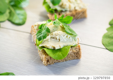 Homemade rye bread with herring paste and arugula on a light wooden table 129797850