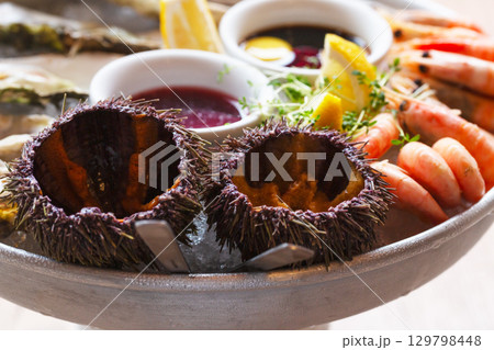 Seafood (oysters, shrimps, sea-urchins, mussels) are decoratively put on ice in a big plate Seafood (oysters, shrimps, sea-urchins, mussels) are decoratively put on ice in a big plate 129798448