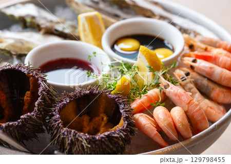 Seafood (oysters, shrimps, sea-urchins, mussels) are decoratively put on ice in a big plate Seafood (oysters, shrimps, sea-urchins, mussels) are decoratively put on ice in a big plate 129798455