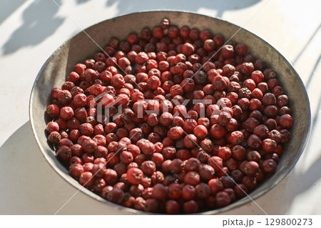 Sichuan red peppercorns in metal bowl sunlit on white surface with shadows 129800273