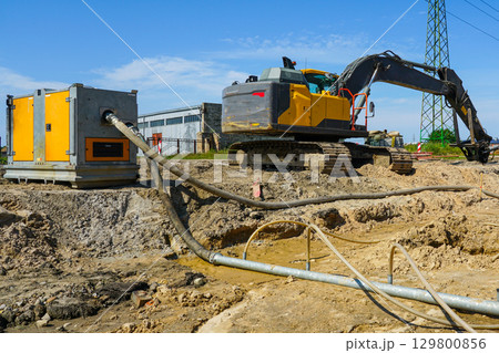 Construction site with dewatering pump, pipes, and excavator during groundwater removal process 129800856