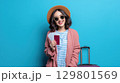 Smiling woman with suitcase holding passport and tickets ready for travel adventure 129801569
