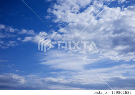 A photorealistic image of a blue sky with white clouds, showcasing a vast expanse of clear blue sky with scattered white clouds of various shapes and sizes. The clouds are fluffy and appear to be 129801685