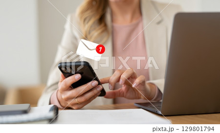 Businesswoman checking new email notification on smartphone at workplace 129801794