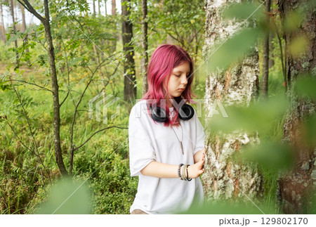 Young relaxed girl listening music leaning against birch in forest 129802170