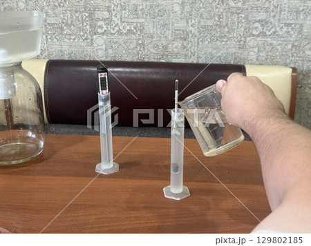 Close up hand of man carefully pouring liquid into graduated cylinde Close up hand of man carefully pouring liquid into graduated cylinde 129802185