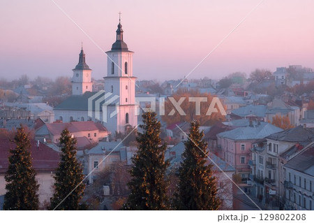 Historic city at dusk with spires. This picturesque skyline shows churches and misty hills. Ideal for travel or serene landscape images. 129802208