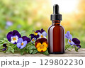 Essential oil bottle with dropper surrounded by pansies on wooden table 129802230