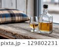Glass and bottle of whisky resting on rustic wooden table 129802231