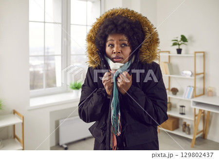 Unhappy young woman feeling cold wearing warm winter jacket indoors 129802437