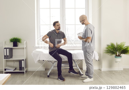 Man sitting in the doctor's office pointing to his stomach during medical examination in clinic Man sitting in the doctor's office pointing to his stomach during medical examination in clinic 129802465