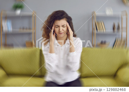 Woman sitting on the couch at home and feeling a dizzy, spinning sensation in her head Woman sitting on the couch at home and feeling a dizzy, spinning sensation in her head 129802468