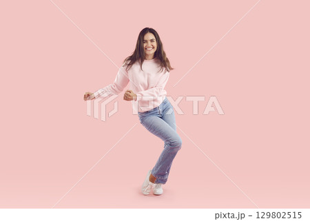 Happy woman in comfortable pink sweatshirt and blue jeans dancing on pink studio background Happy woman in comfortable pink sweatshirt and blue jeans dancing on pink studio background 129802515