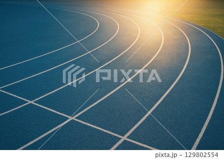 Blue running track curving into sunlight with glowing morning atmosphere, symbolizing sports motivation and high resolution sports photography 129802554