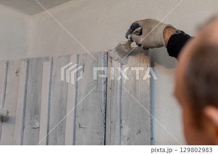 Individual Skillfully Applying Paint to Rustic Wall Panels for a Stylish Aesthetic Appeal 129802983