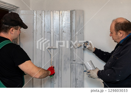 A group of men skillfully painting a wall with rollers and brushes for a fresh look A group of men skillfully painting a wall with rollers and brushes for a fresh look 129803033