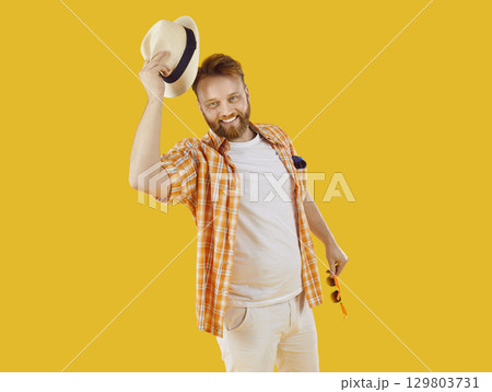 Man with sunglasses and beach hat is going on summer holiday trip isolated on yellow background Man with sunglasses and beach hat is going on summer holiday trip isolated on yellow background 129803731