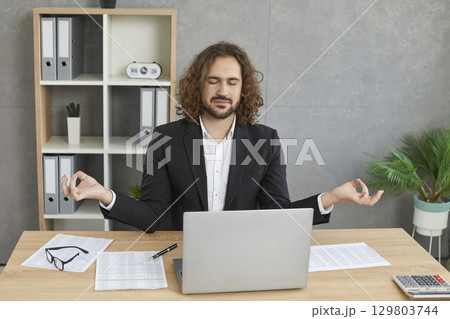 Young relaxed business man meditating and having a rest in the office on his workplace. 129803744